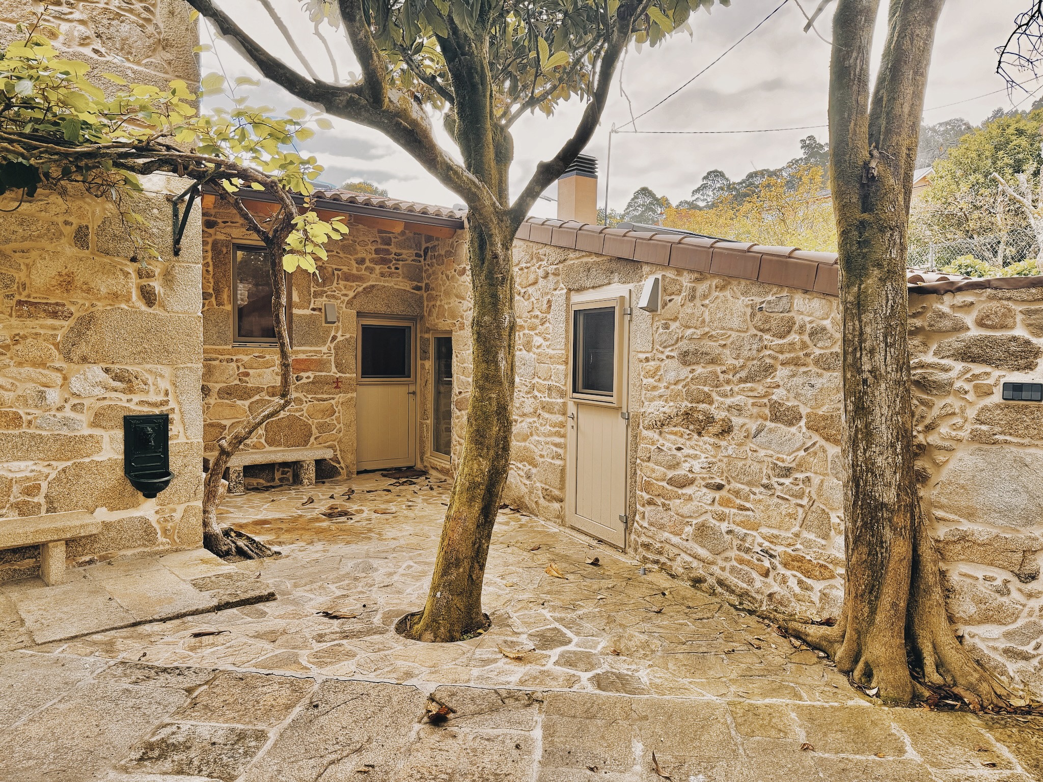 Patio de piedra con vivienda rehabilitada y arbolado